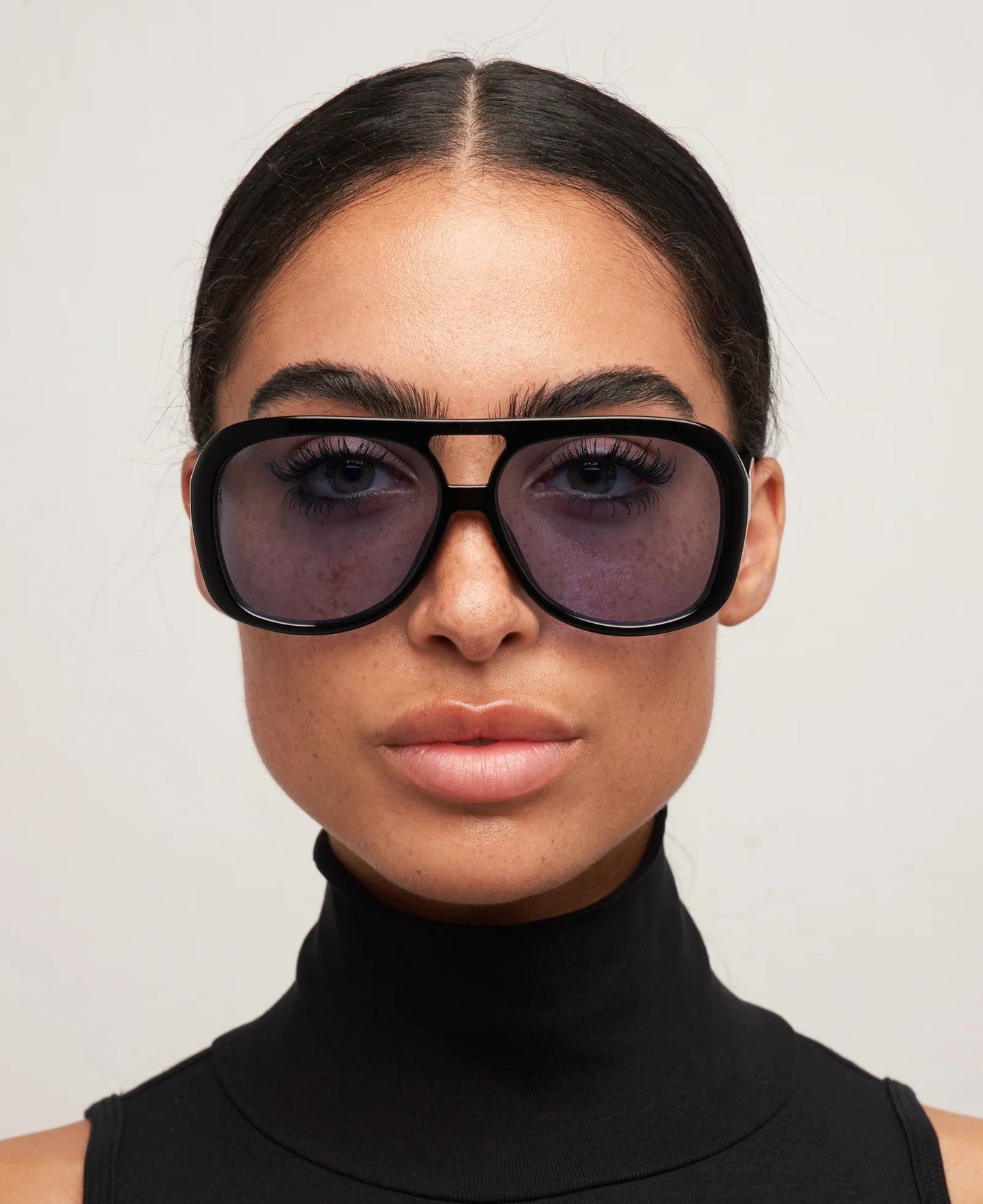 Person wearing large black sunglasses with a plain background