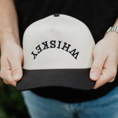 Person holding a cap with 'WHISKEY' text against a dark background