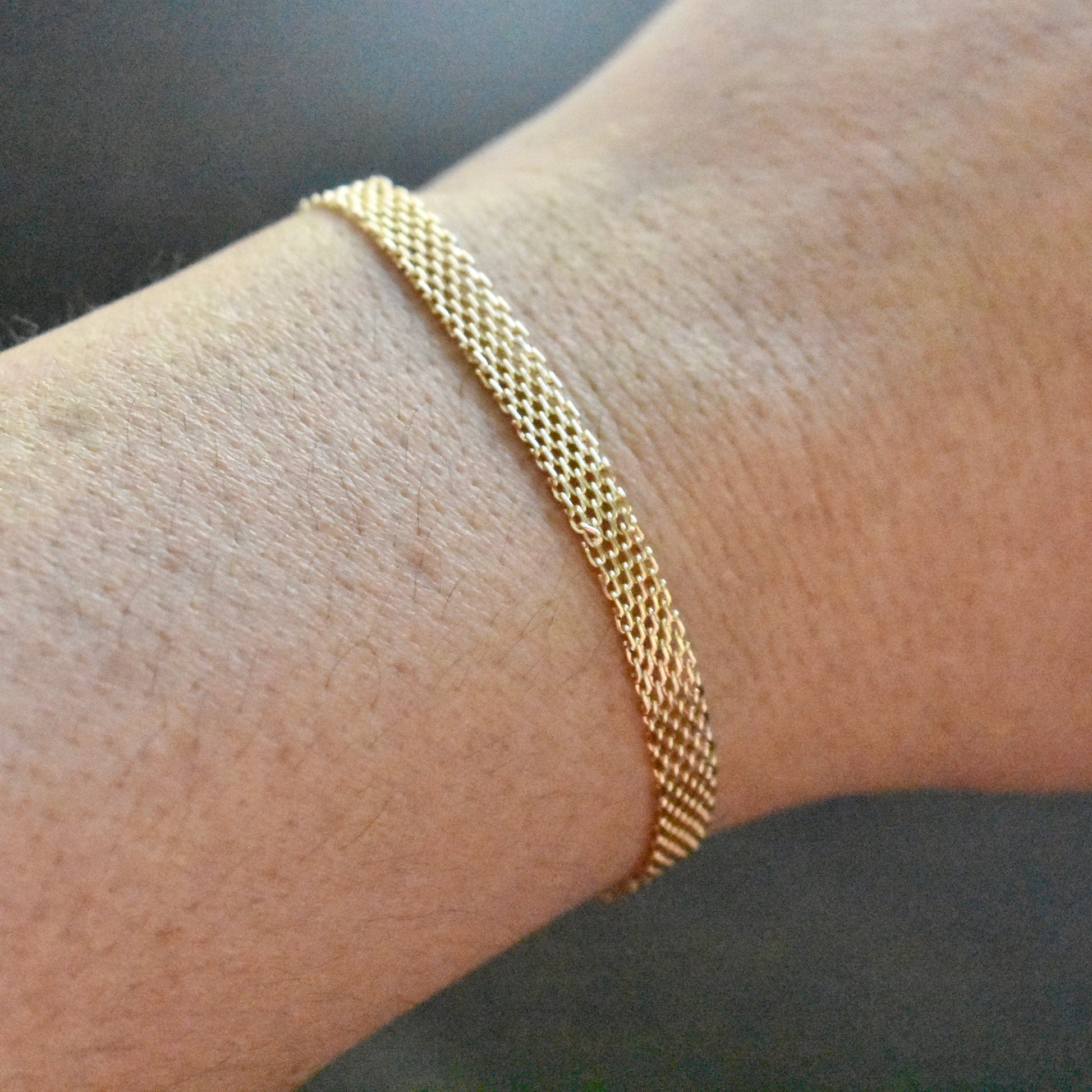 Gold bracelet on a wrist against a neutral background