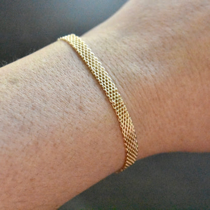 Gold bracelet on a wrist against a neutral background