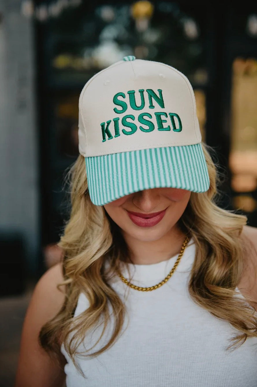 Person wearing a cap with 'SUN KISSED' text in an outdoor setting