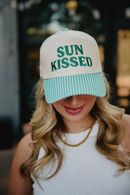 Person wearing a cap with 'SUN KISSED' text in an outdoor setting