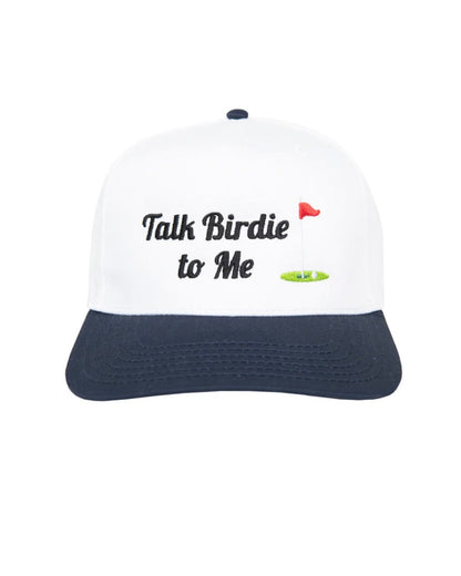 A white and navy blue baseball cap with a golf-themed graphic on the front that reads 'Talk Birdie to Me' alongside a small red flag and green putting green illustration.