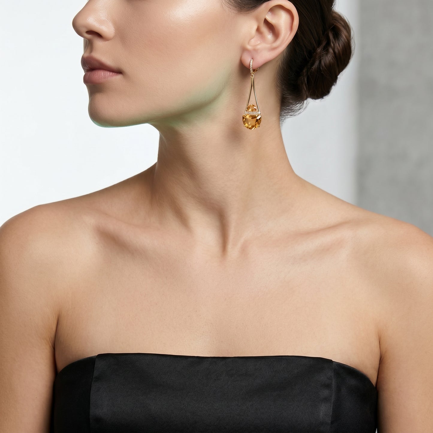 Close-up of a woman wearing gold earrings with a black strapless top against a neutral background