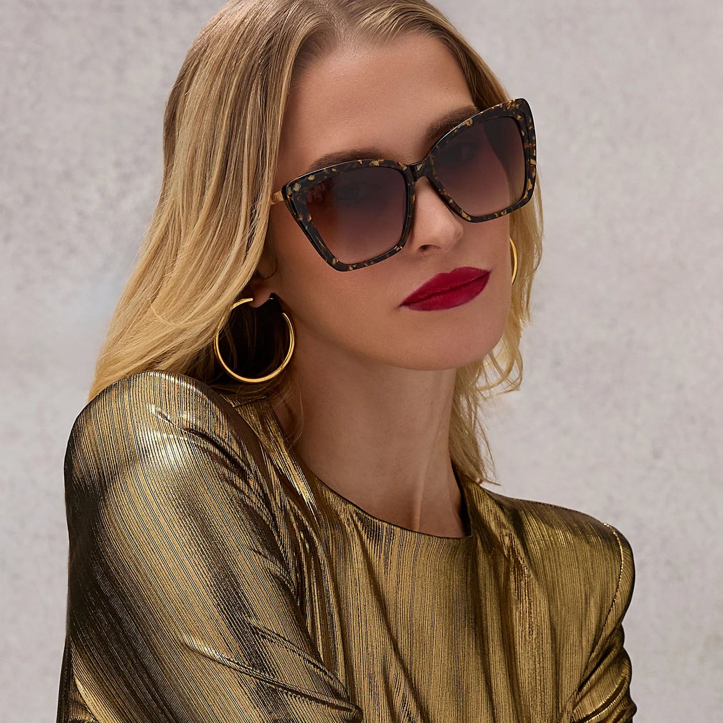 Woman wearing sunglasses and a gold outfit against a neutral background