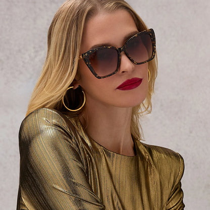 Woman wearing sunglasses and a gold outfit against a neutral background