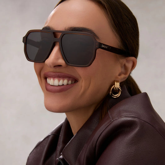 Woman wearing sunglasses and a brown leather jacket with a neutral background