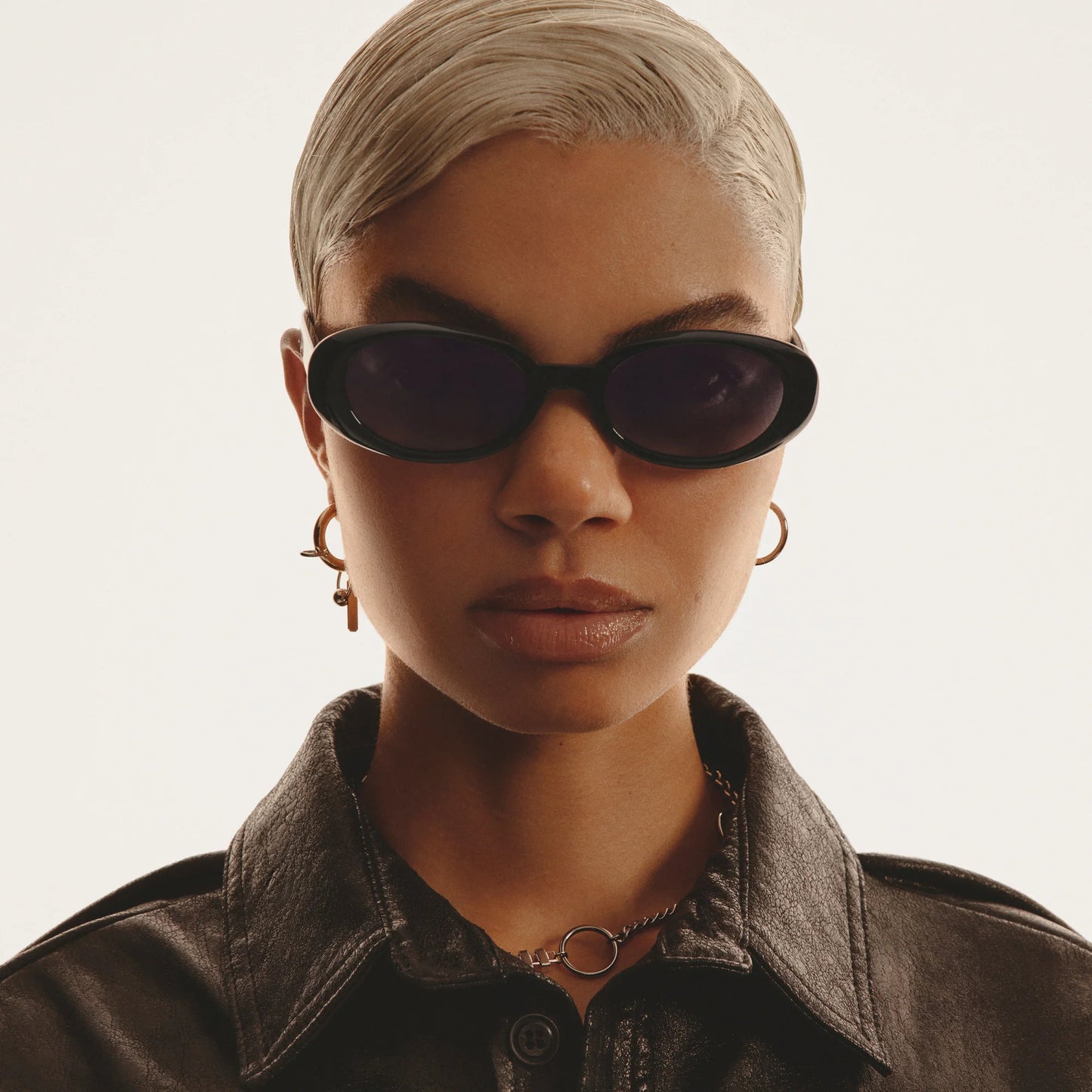 Person wearing sunglasses and a dark jacket on a neutral background