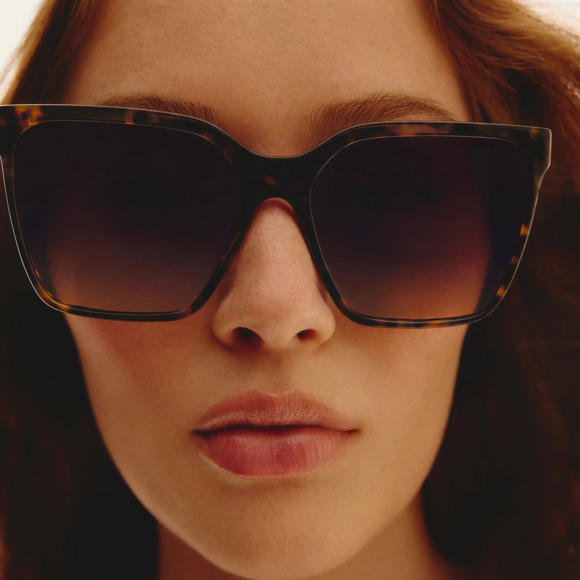 Close-up of a person wearing tortoiseshell sunglasses with a blurred background