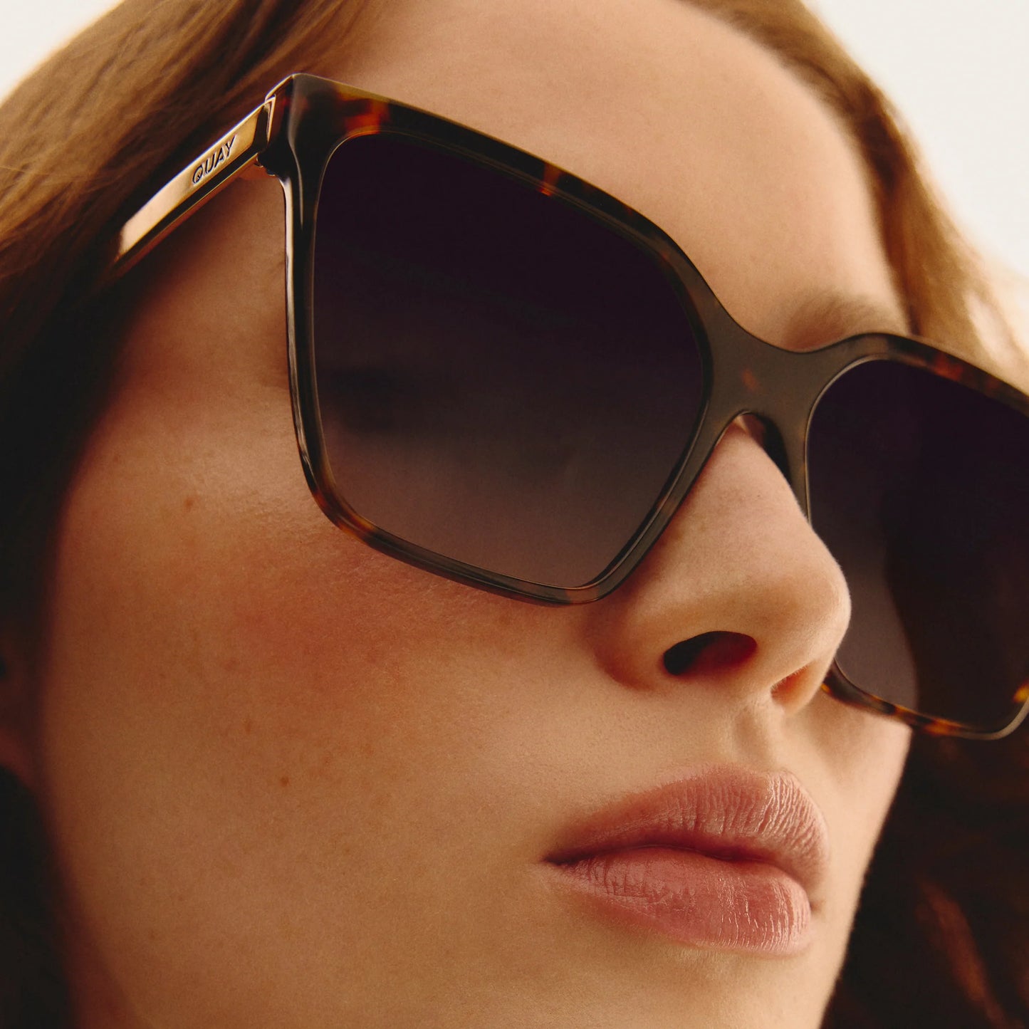 Close-up of a person wearing tortoiseshell sunglasses with a blurred background
