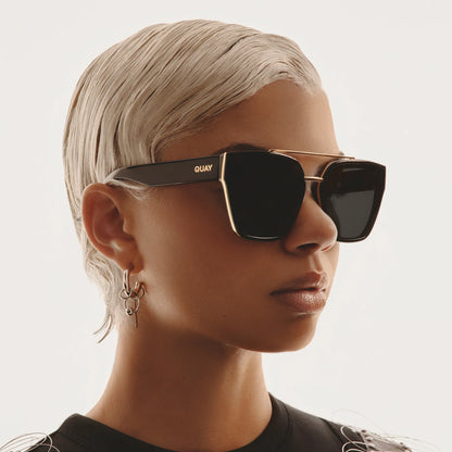 Person wearing black sunglasses with gold frame on a neutral background