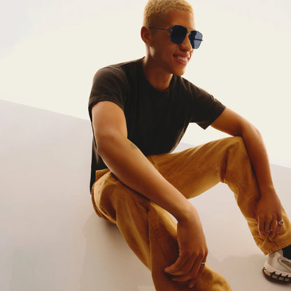 Person wearing sunglasses and casual clothing sitting on a white surface