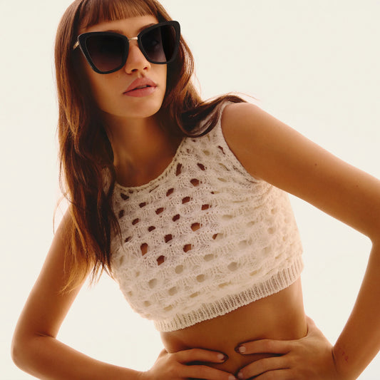 Woman wearing a white crochet top and sunglasses against a light background