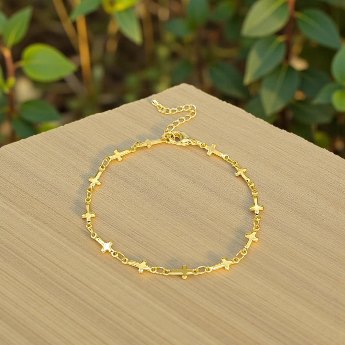 Gold bracelet with cross patterns on a wooden surface with green foliage in the background