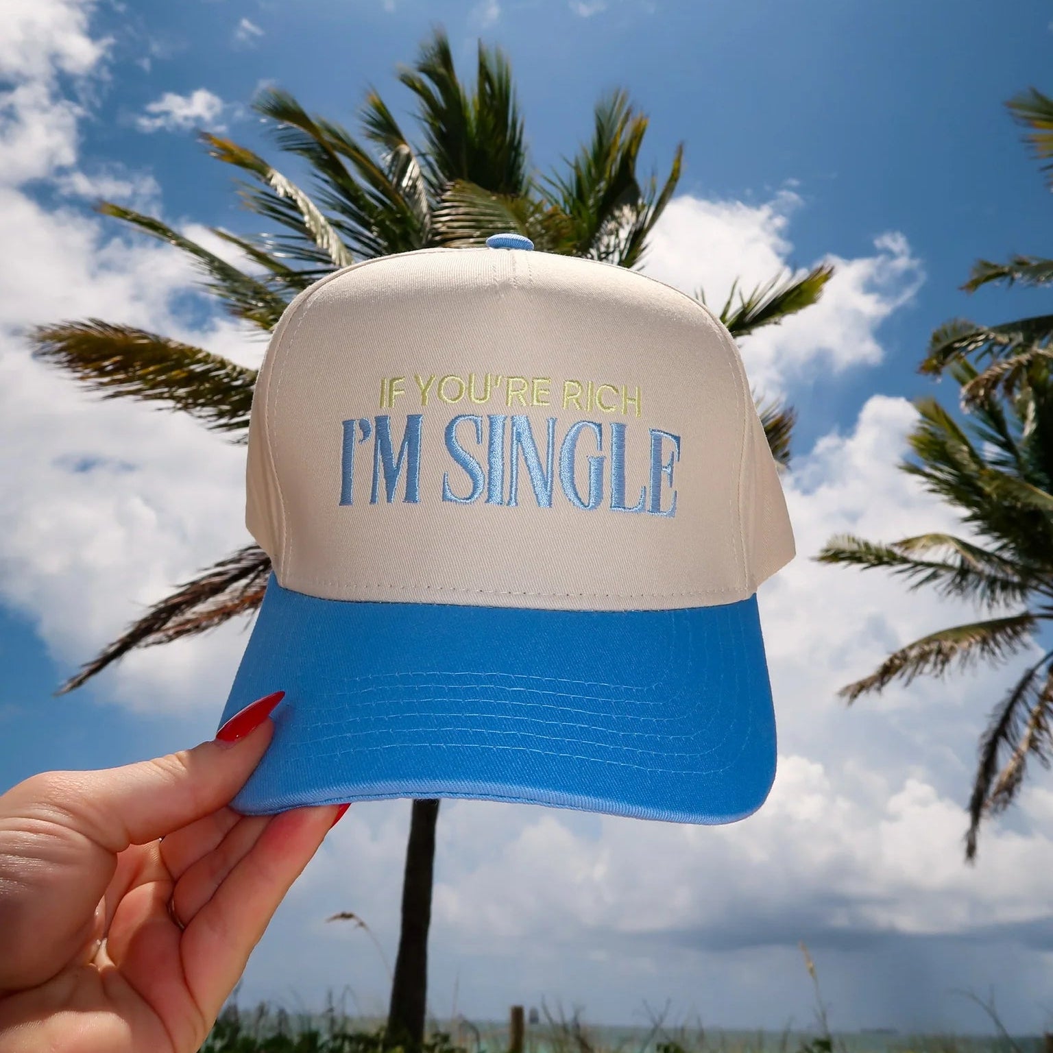 Beige and blue cap with 'I'm Single' text held against a palm tree and blue sky background