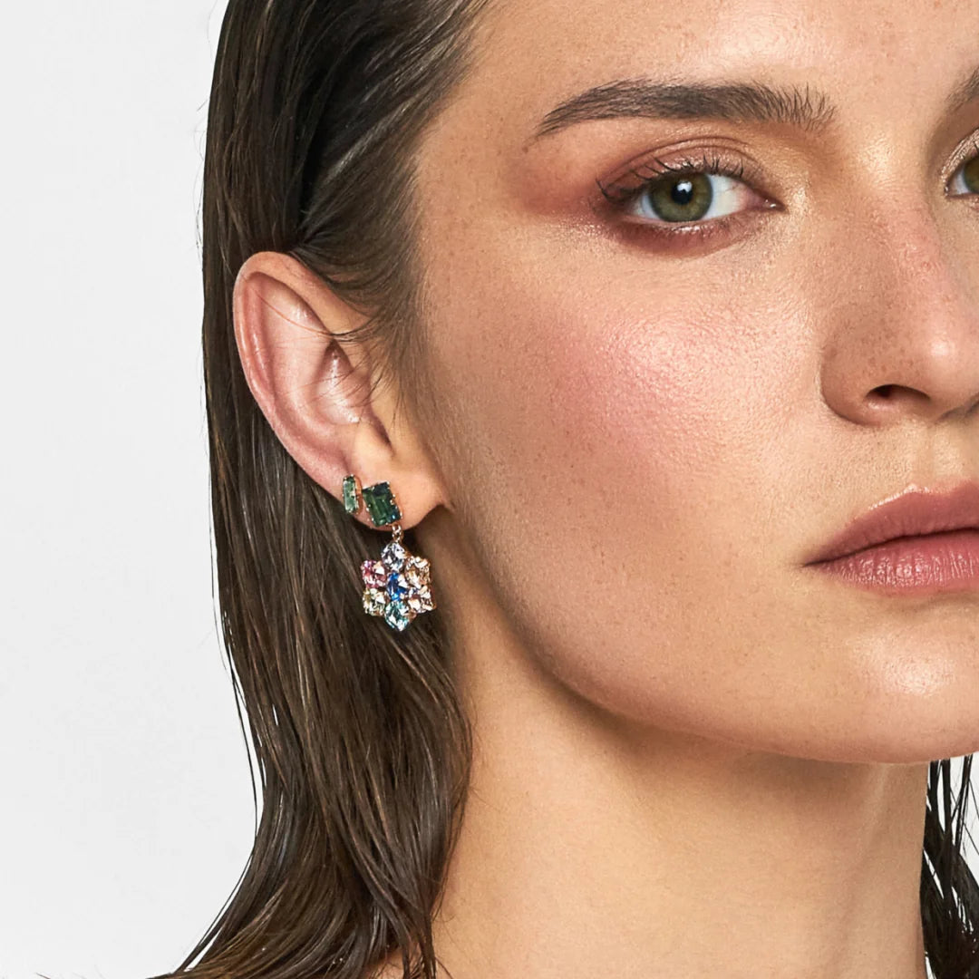 Close-up of a woman wearing a floral earring with green gemstones on a white background
Material: Sterling Silver, Rose Gold Plated, multi-colored Swarovski Crystals

Color: sterling silver, yellow gold, pink, blue, green, purple

Measurement: 3 mm thickness, 2.5 cm length, 1.5 cm width