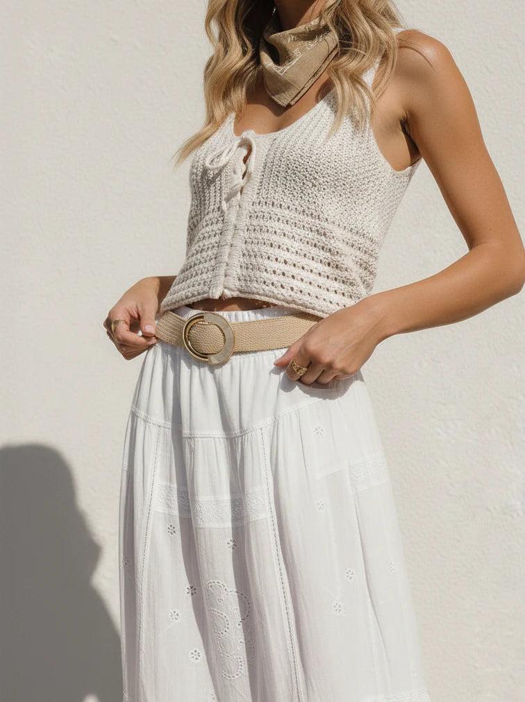 Woman wearing a white crochet top and skirt with a beige belt against a light background