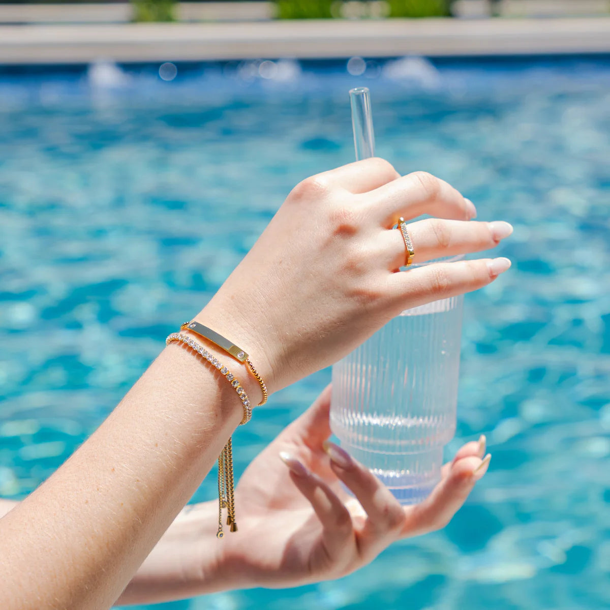 Hand holding a clear plastic cup with a straw by a pool