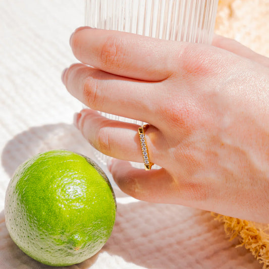 Hand with a ring holding a green lime next to a glass of water.