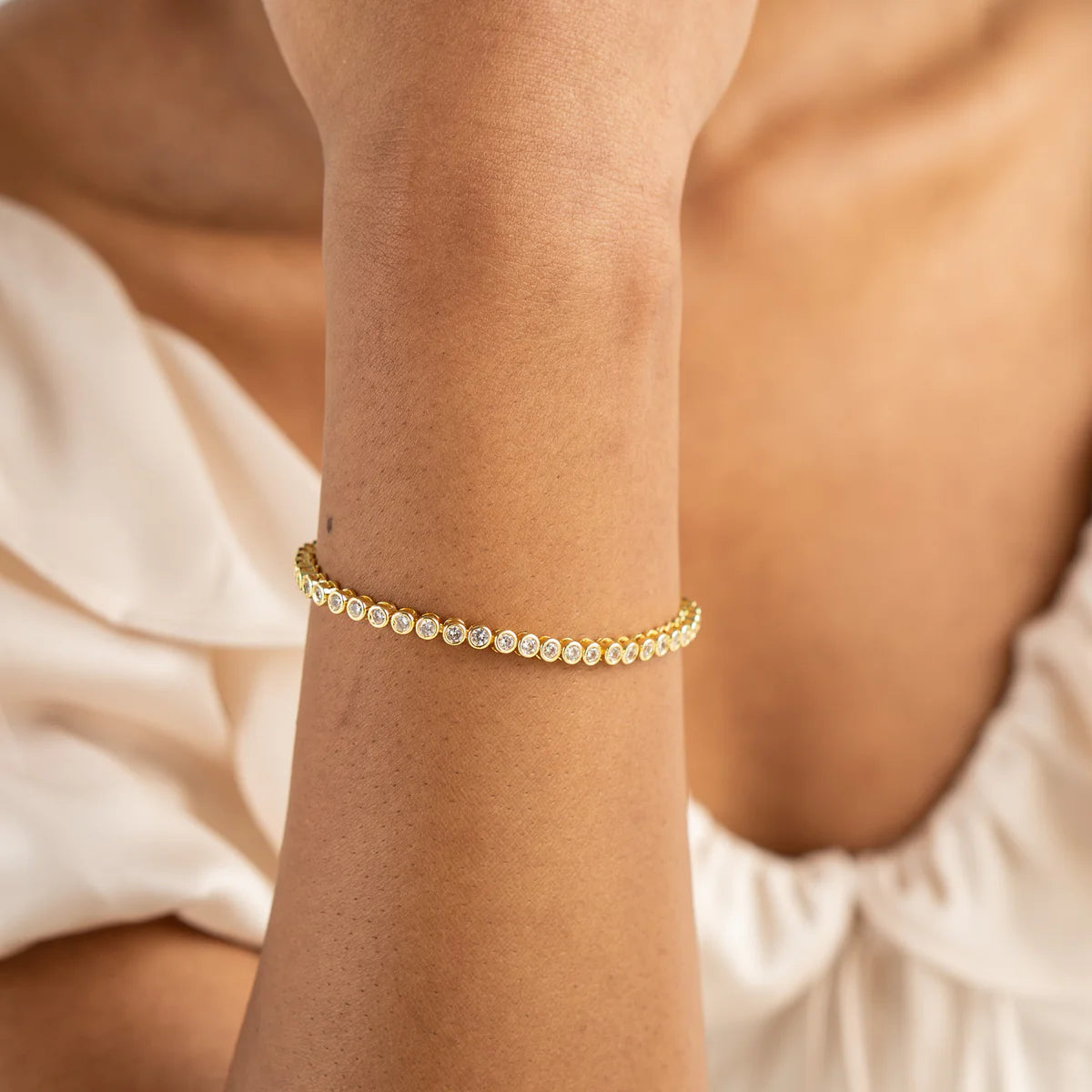 Gold bracelet on a wrist with a neutral background