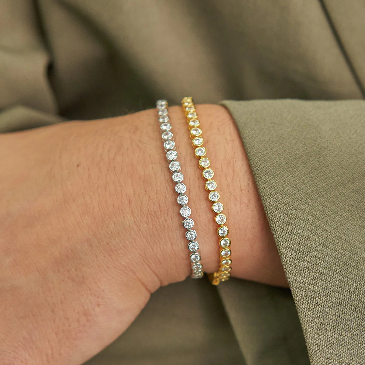 Two diamond bracelets on a person's wrist with a blurred background