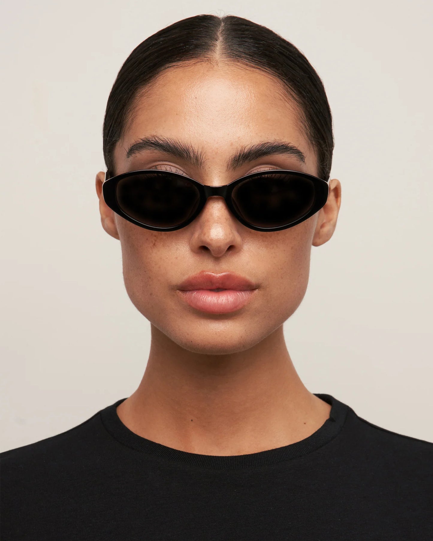 Person wearing black sunglasses and a black shirt against a plain background