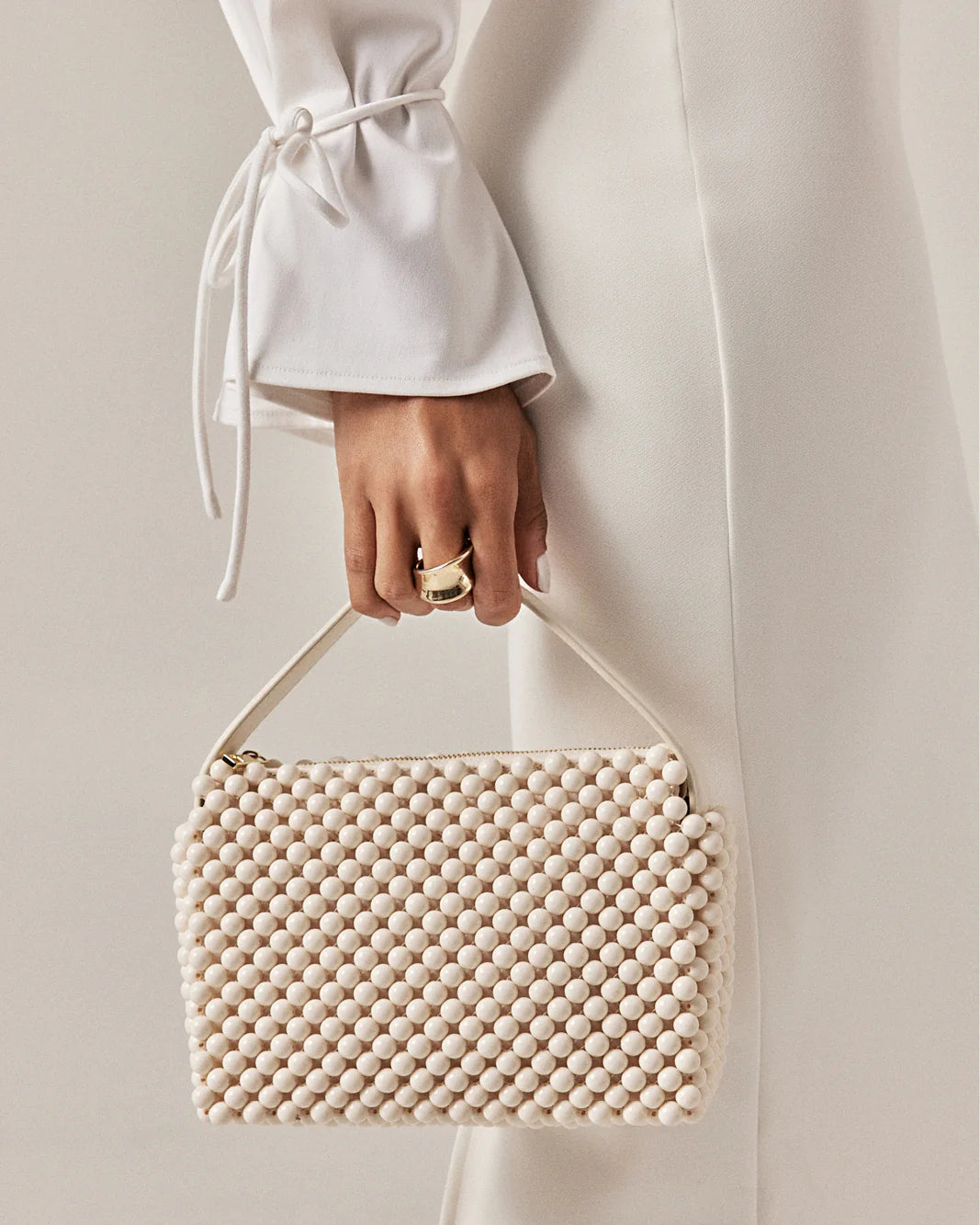 Hand holding a beige beaded handbag against a neutral background