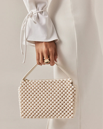 Hand holding a beige beaded handbag against a neutral background