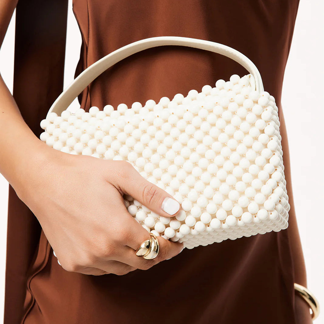 White beaded handbag held by a person wearing a brown dress.