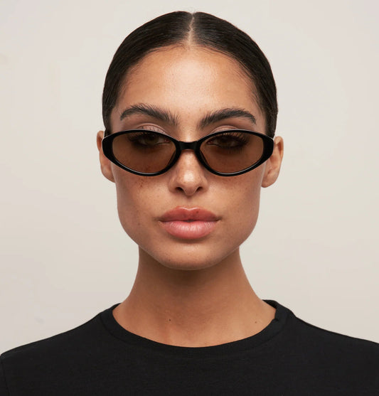 Person wearing black sunglasses and a black shirt against a light background