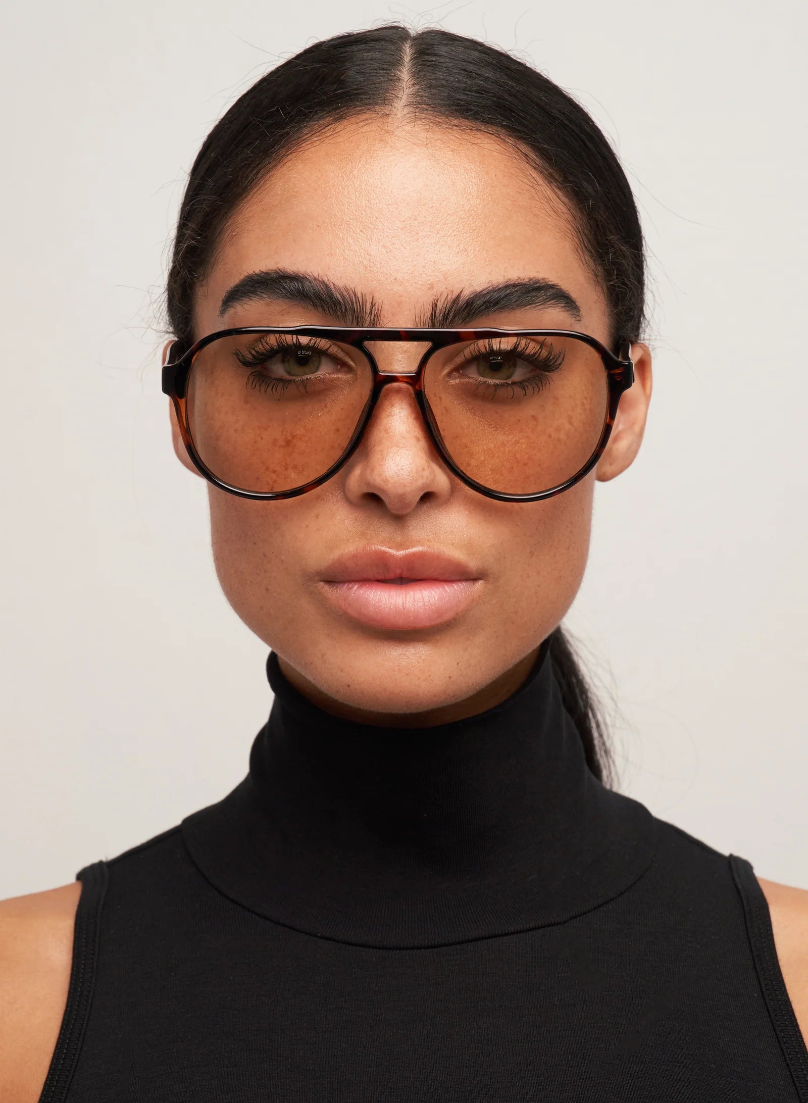 Woman wearing a black turtleneck and sunglasses against a plain background