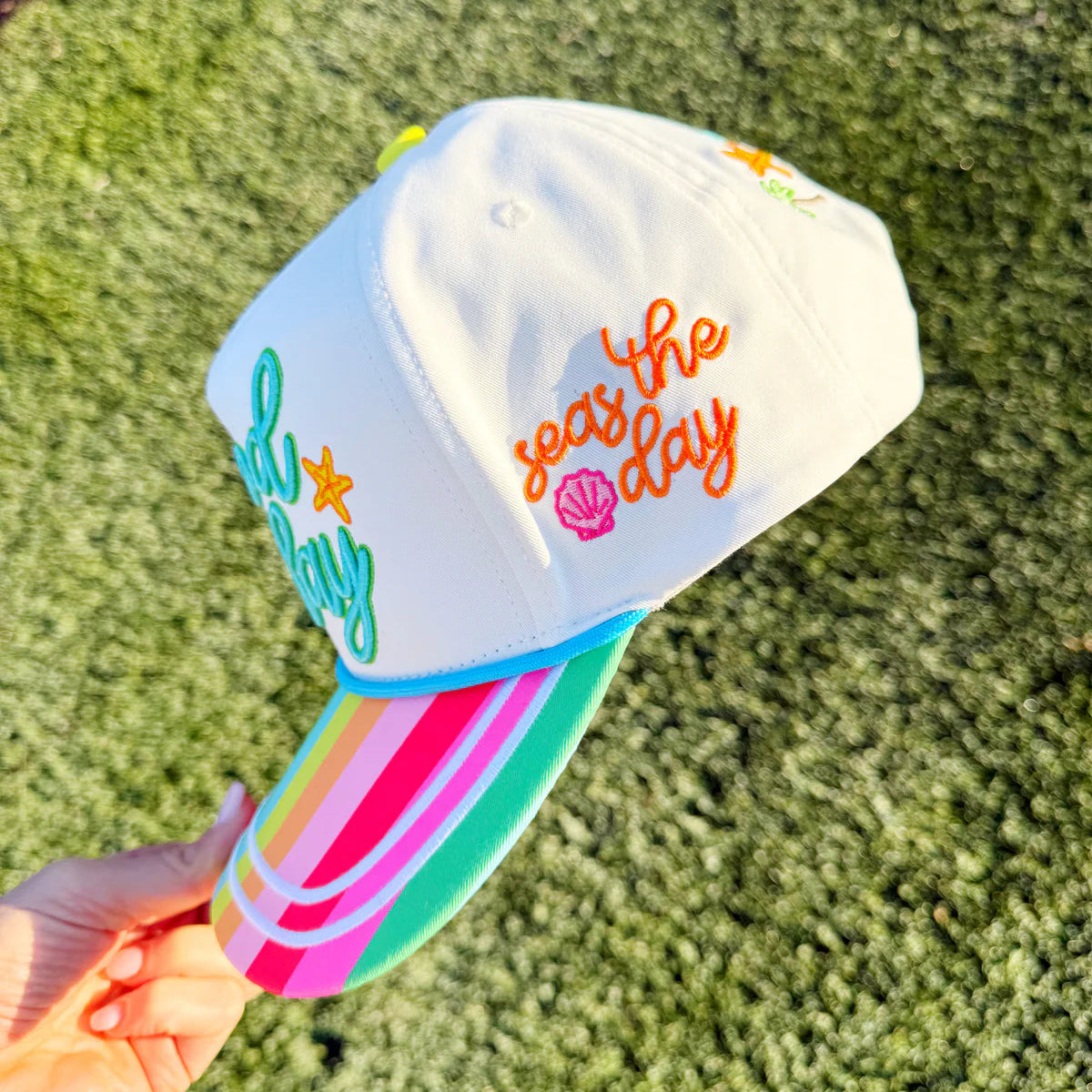 Colorful cap with 'Do the seas the day' text held by a hand on grass