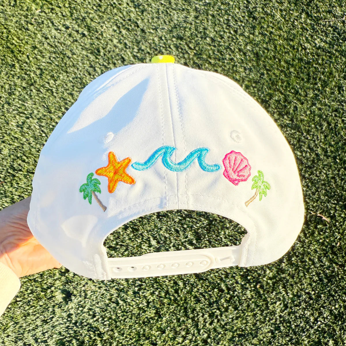 White cap with colorful embroidered designs on a grassy background