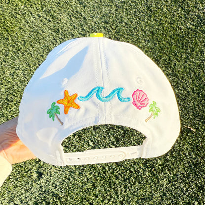 White cap with colorful embroidered designs on a grassy background