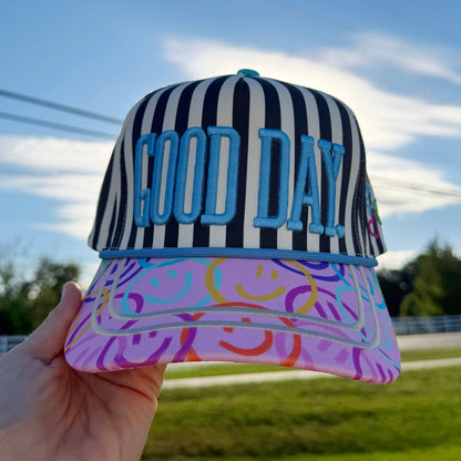 Striped cap with 'GOOD DAY' text held against a blue sky.