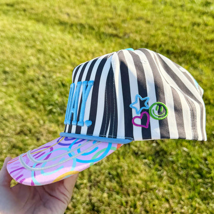 Striped cap with colorful text and designs held in front of a grassy background