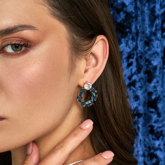 Close-up of a woman wearing a deep green swarovski crystal earring against a blue textured background