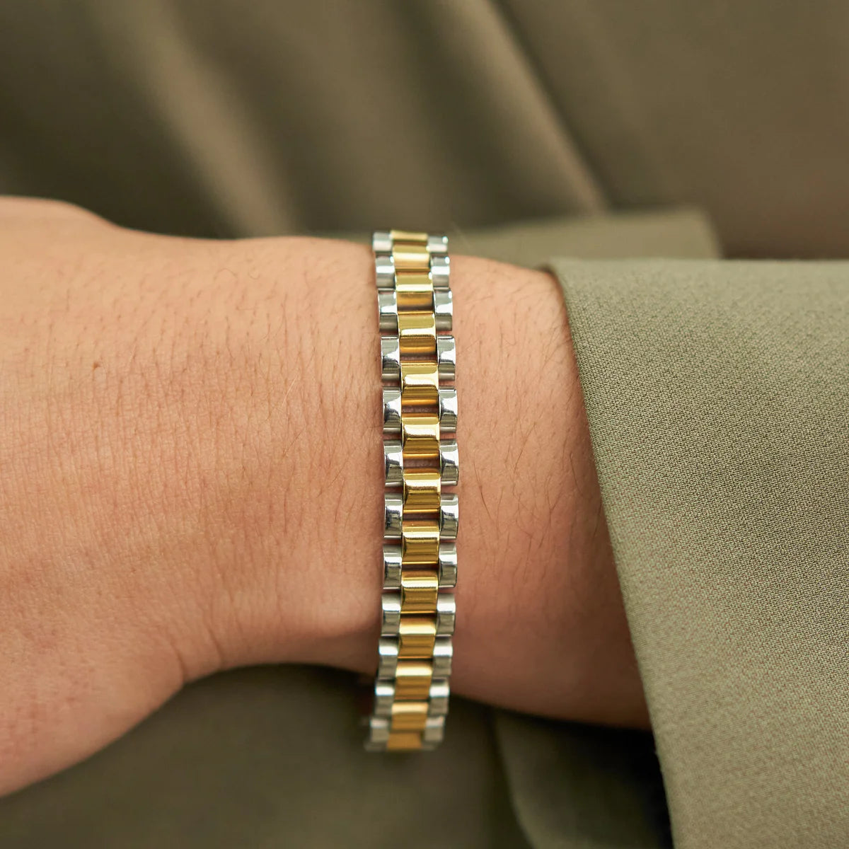 Close-up of a wrist wearing a silver and gold bracelet against a green background