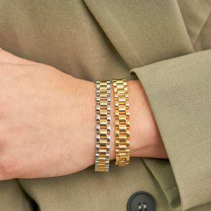 Close-up of a wrist wearing two gold bracelets with a neutral background