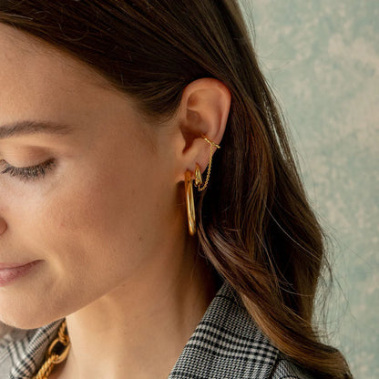 Close-up of a woman wearing gold hoop earrings with a neutral background