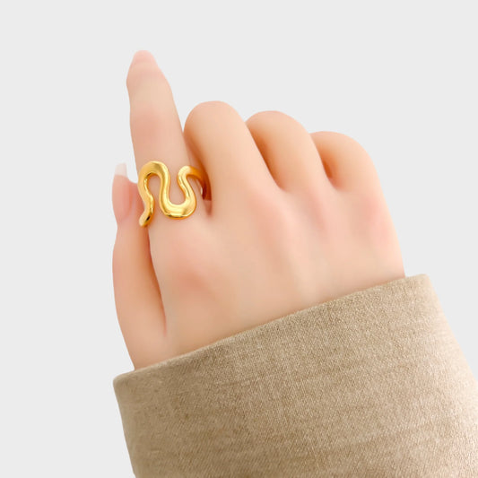 Gold snake-shaped ring on a hand against a light background