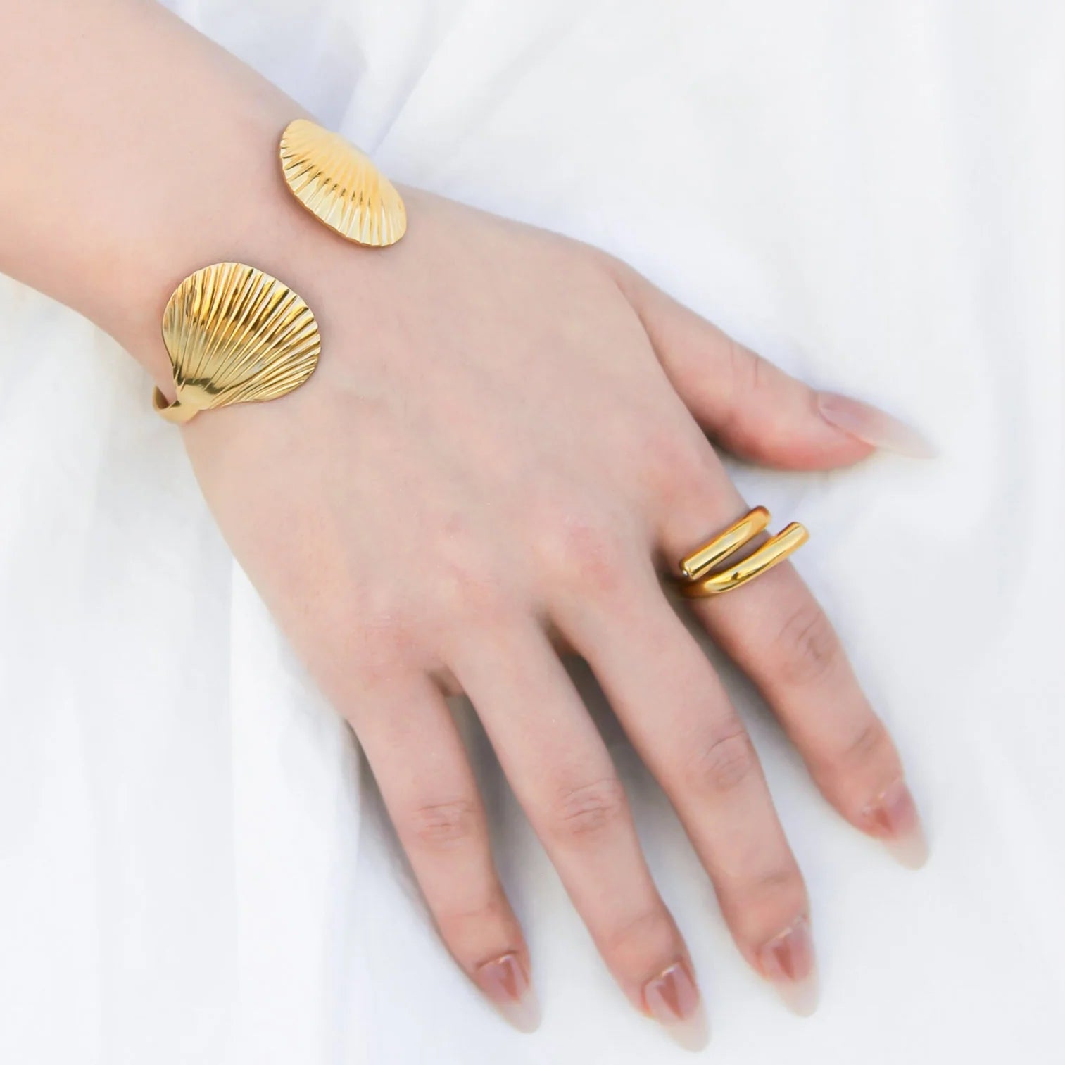 Gold shell-shaped bracelet and ring on a hand against a white background