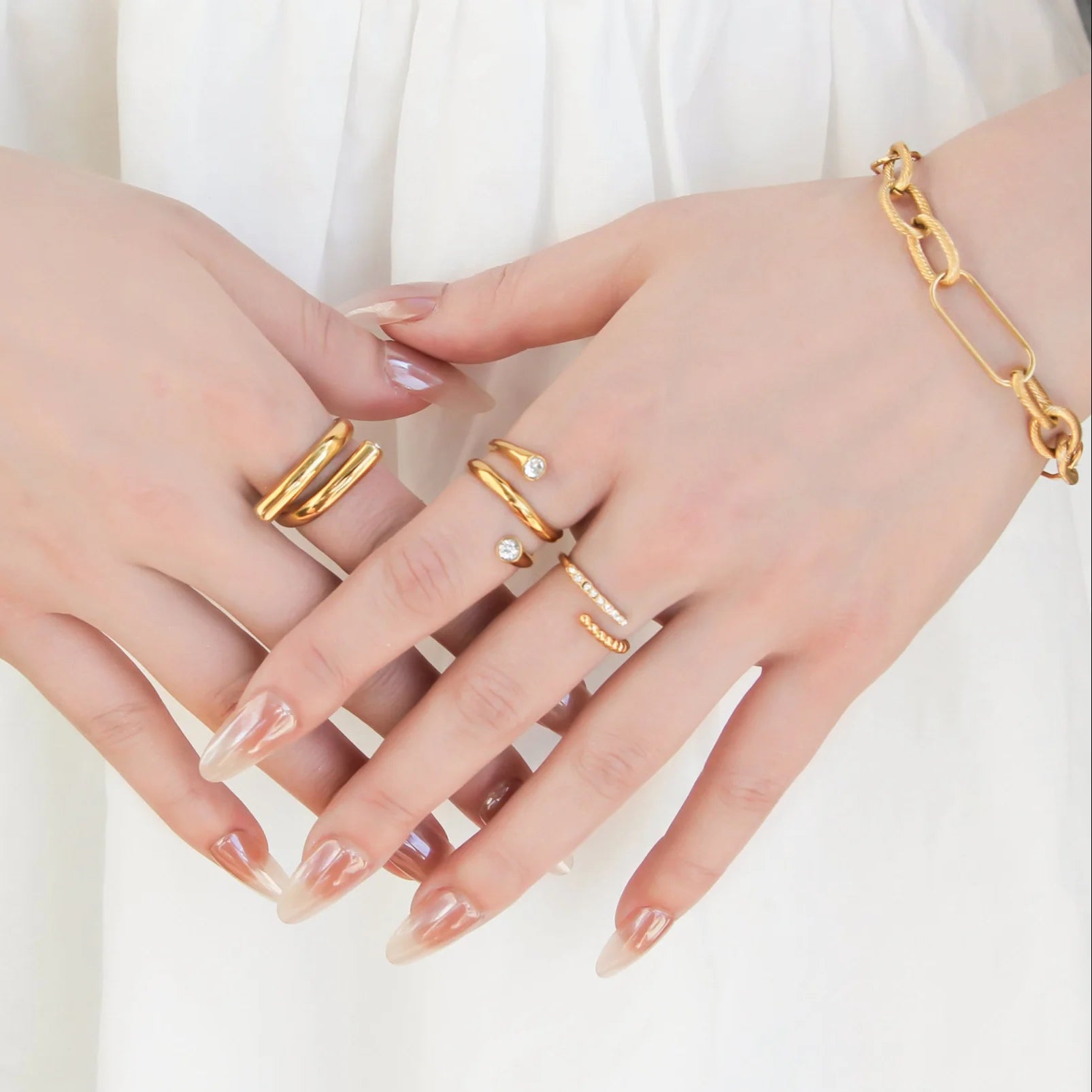 Gold rings and bracelet on a hand against a white background