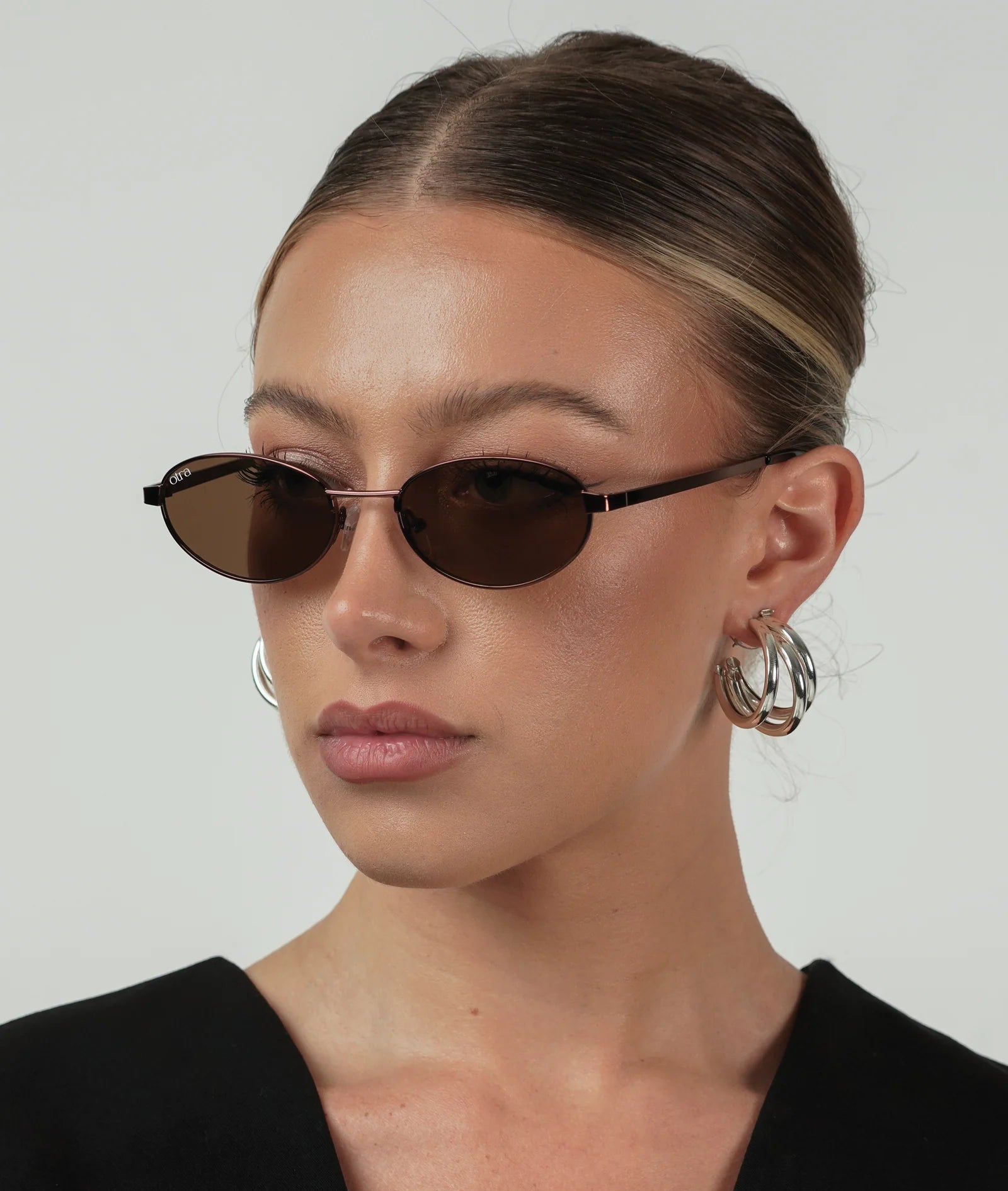 Woman wearing sunglasses and hoop earrings against a plain background