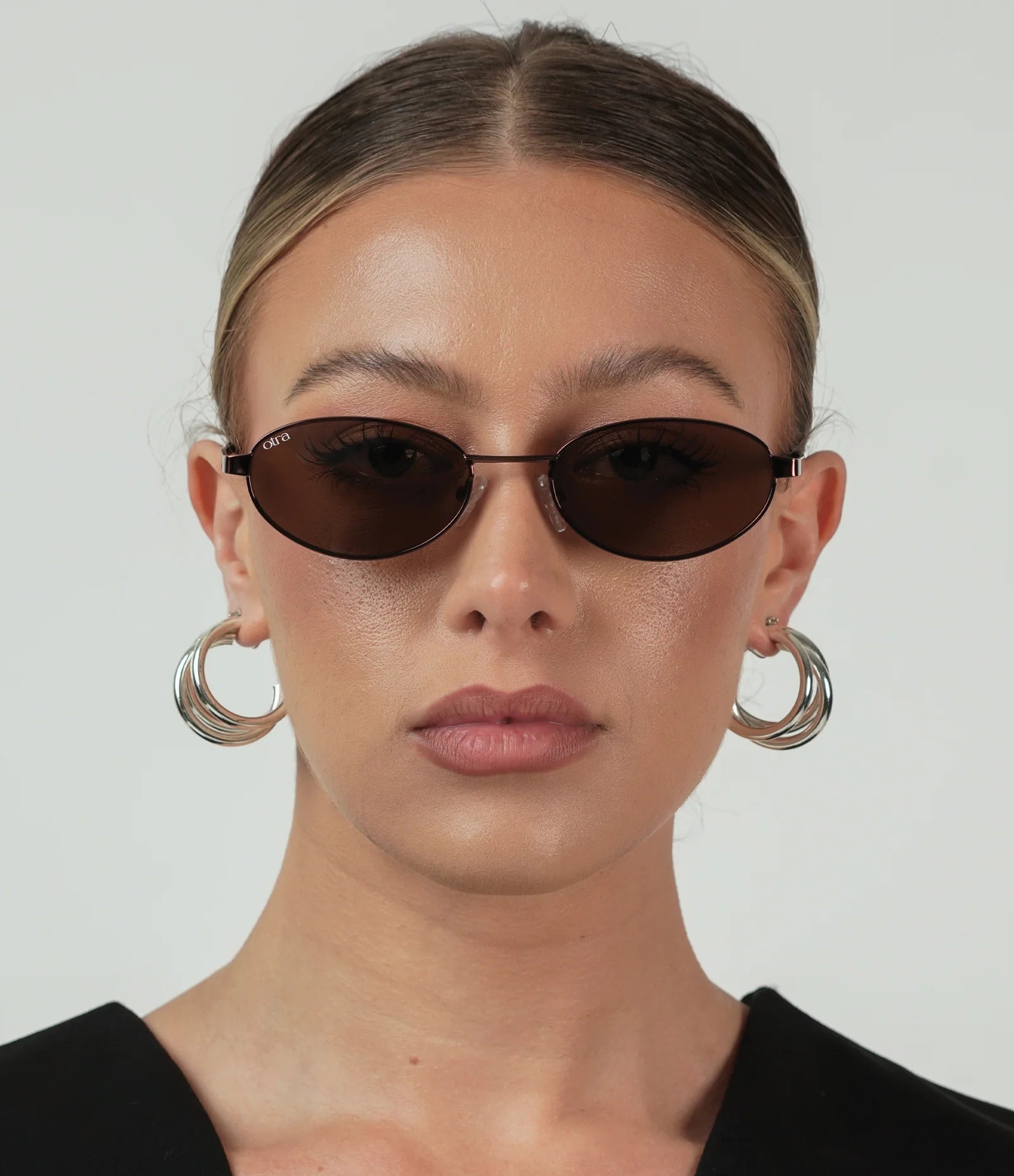 Woman wearing dark sunglasses and hoop earrings against a plain background
