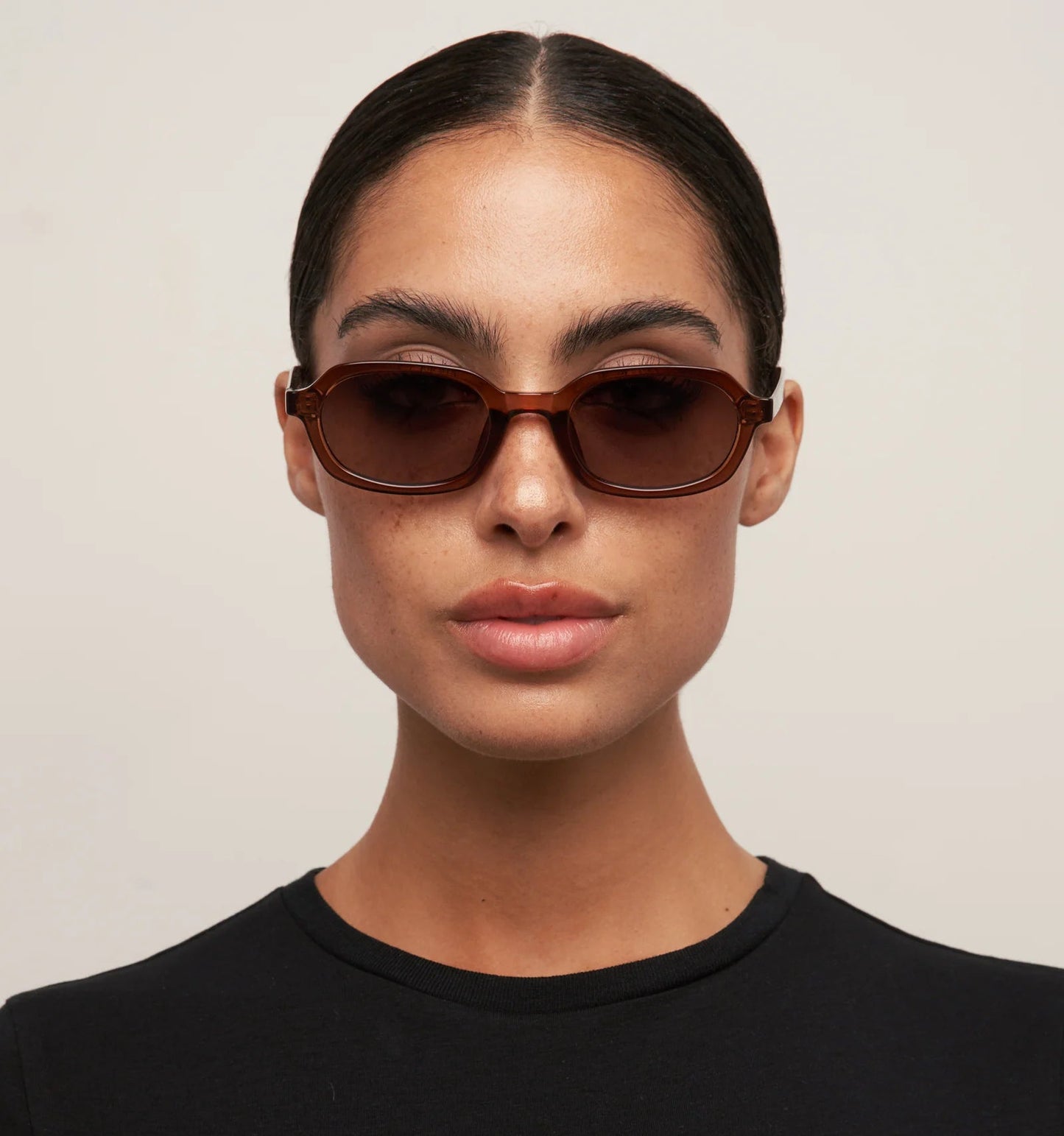 Person wearing brown sunglasses and a black shirt against a plain background