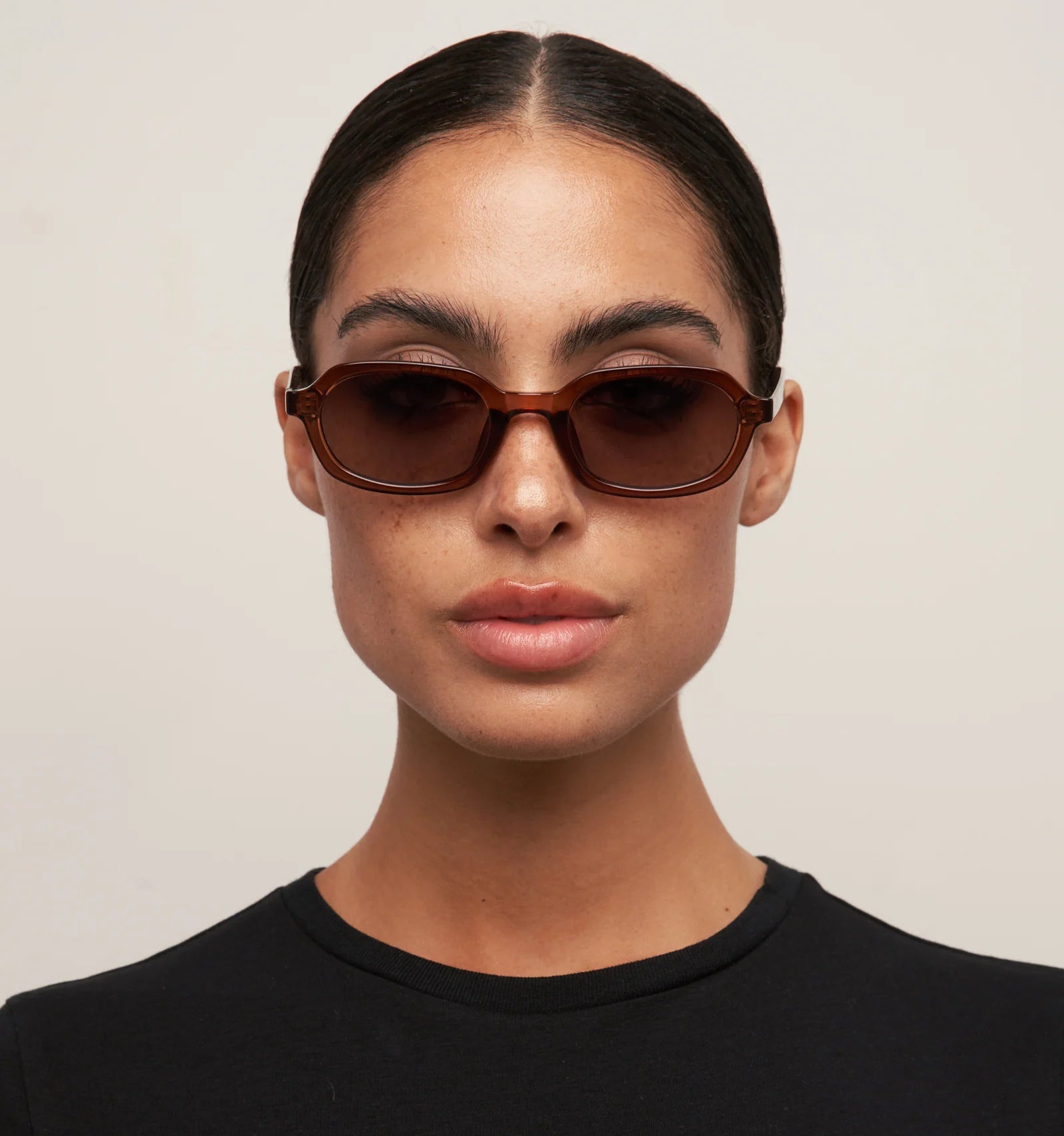 Person wearing brown sunglasses and a black shirt against a plain background