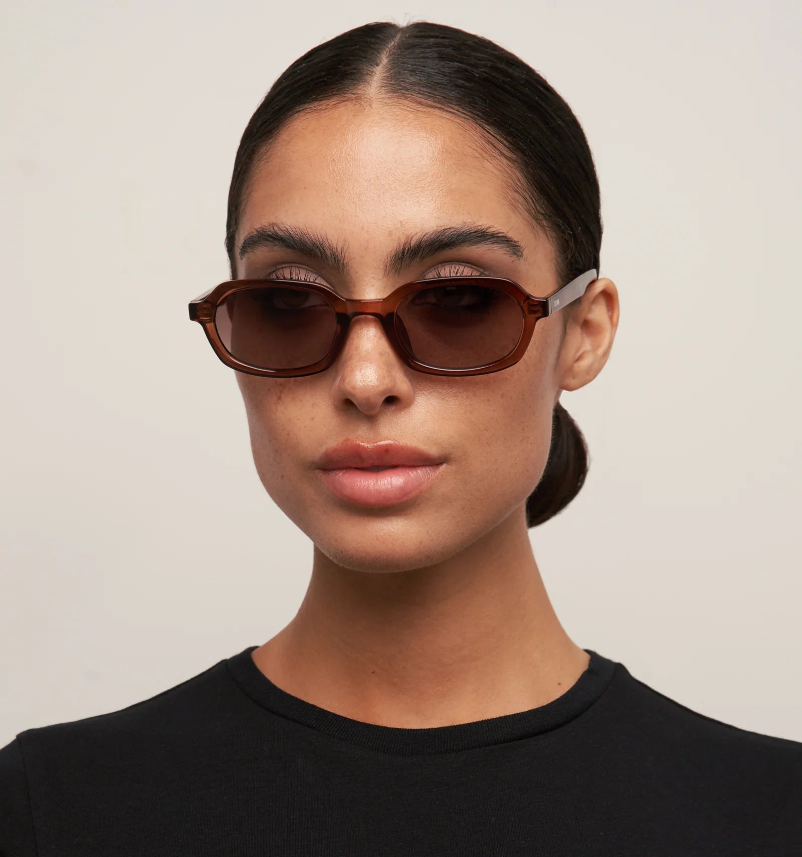 Woman wearing brown sunglasses with a plain background