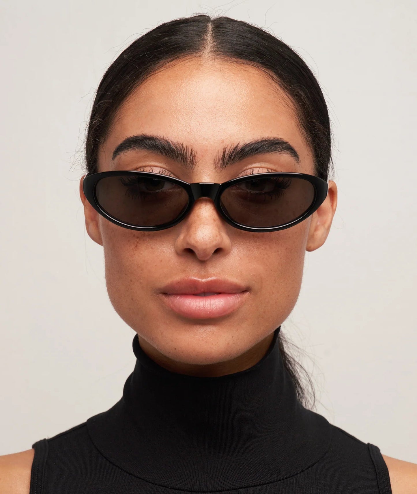 Woman wearing black sunglasses and a black turtleneck against a light gray background