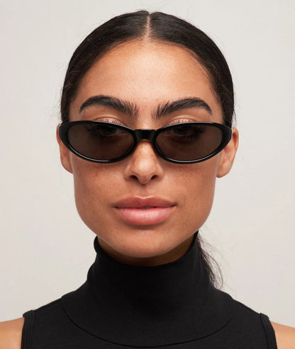 Woman wearing black sunglasses and a black turtleneck against a light gray background